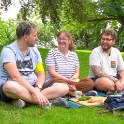 zwei Männer und eine Frau sitzen auf einer Wiese und lachen
