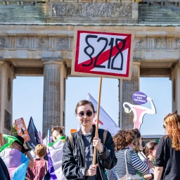 Eine junge Demonstrantin hält während eines Protest vor dem Brandenburger Tor ein Schild mit der durchgestrichenen Aufschrift "§ 218" in die Höhe.